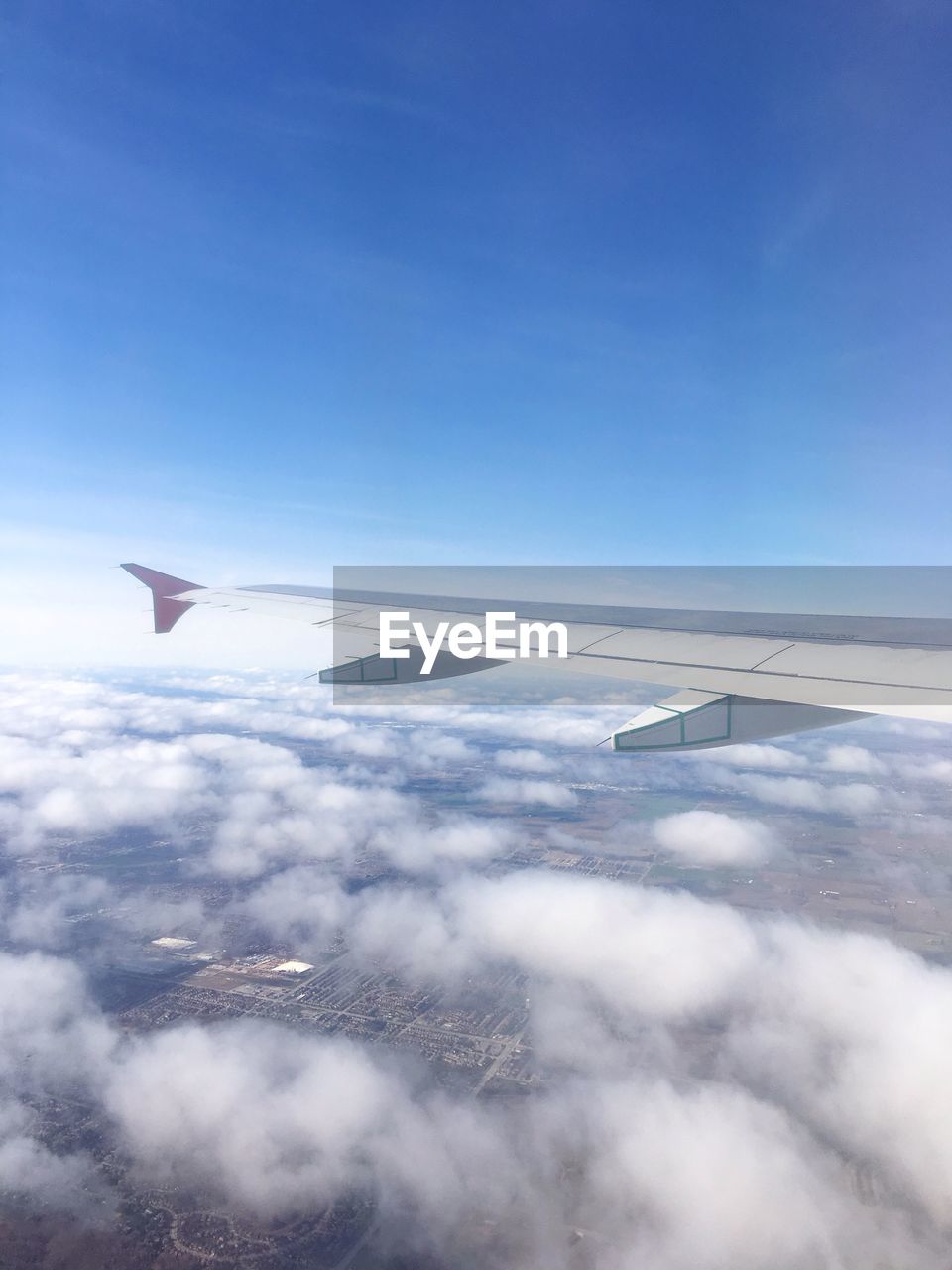 Cropped image of airplane flying over landscape against blue sky