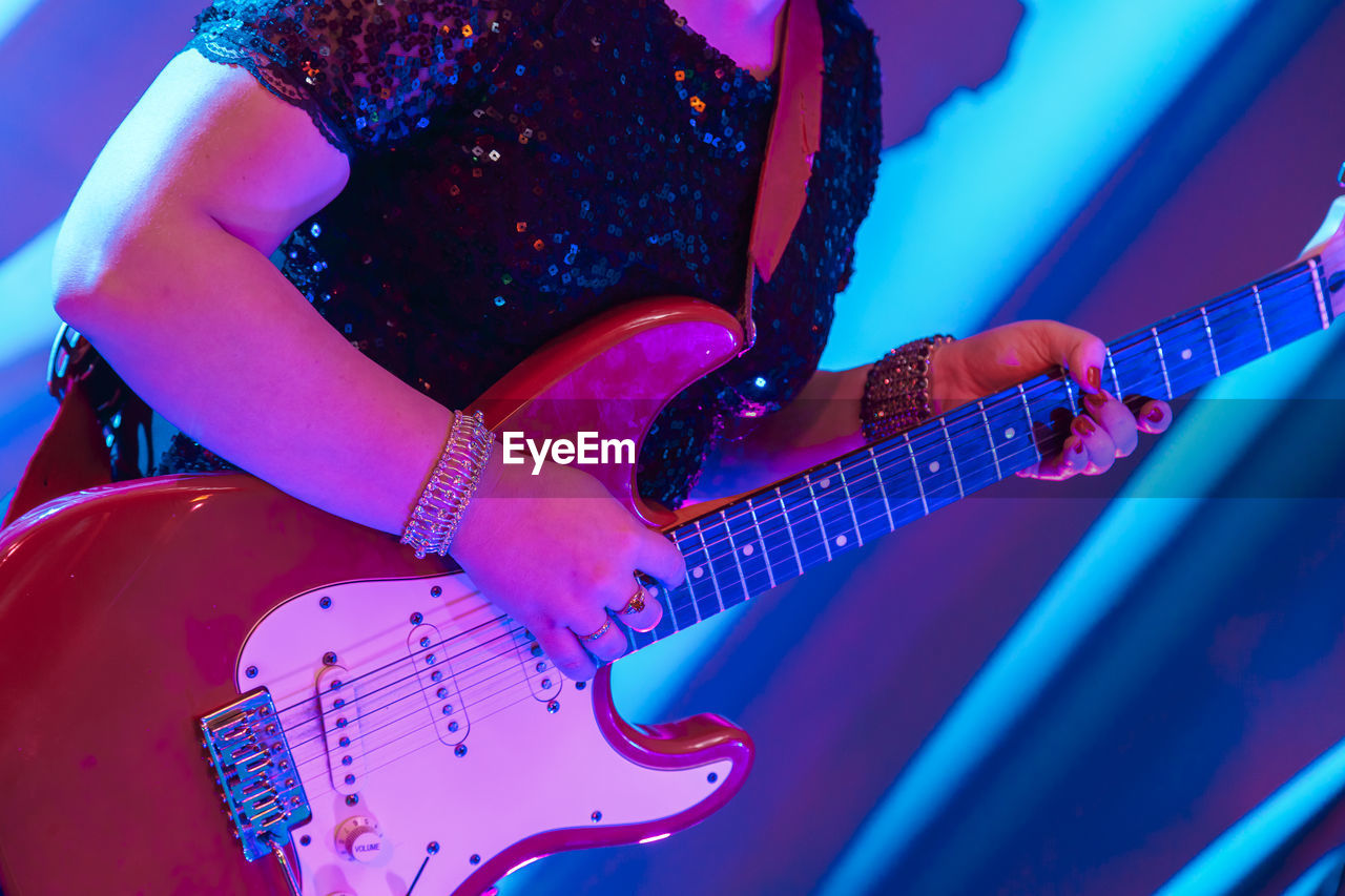 MIDSECTION OF WOMAN PLAYING GUITAR AT NIGHTCLUB