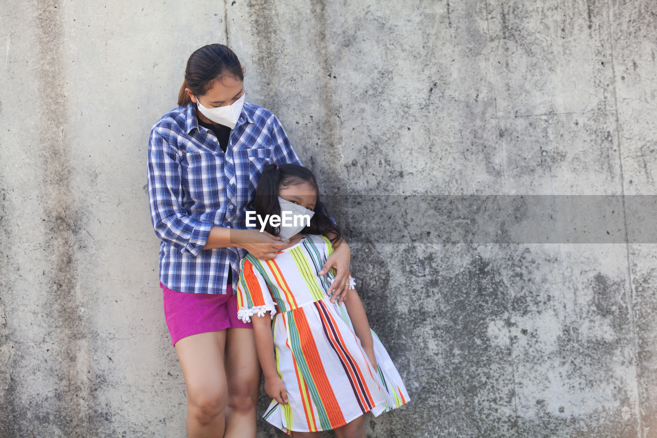 GIRL HOLDING WOMEN STANDING BY WALL