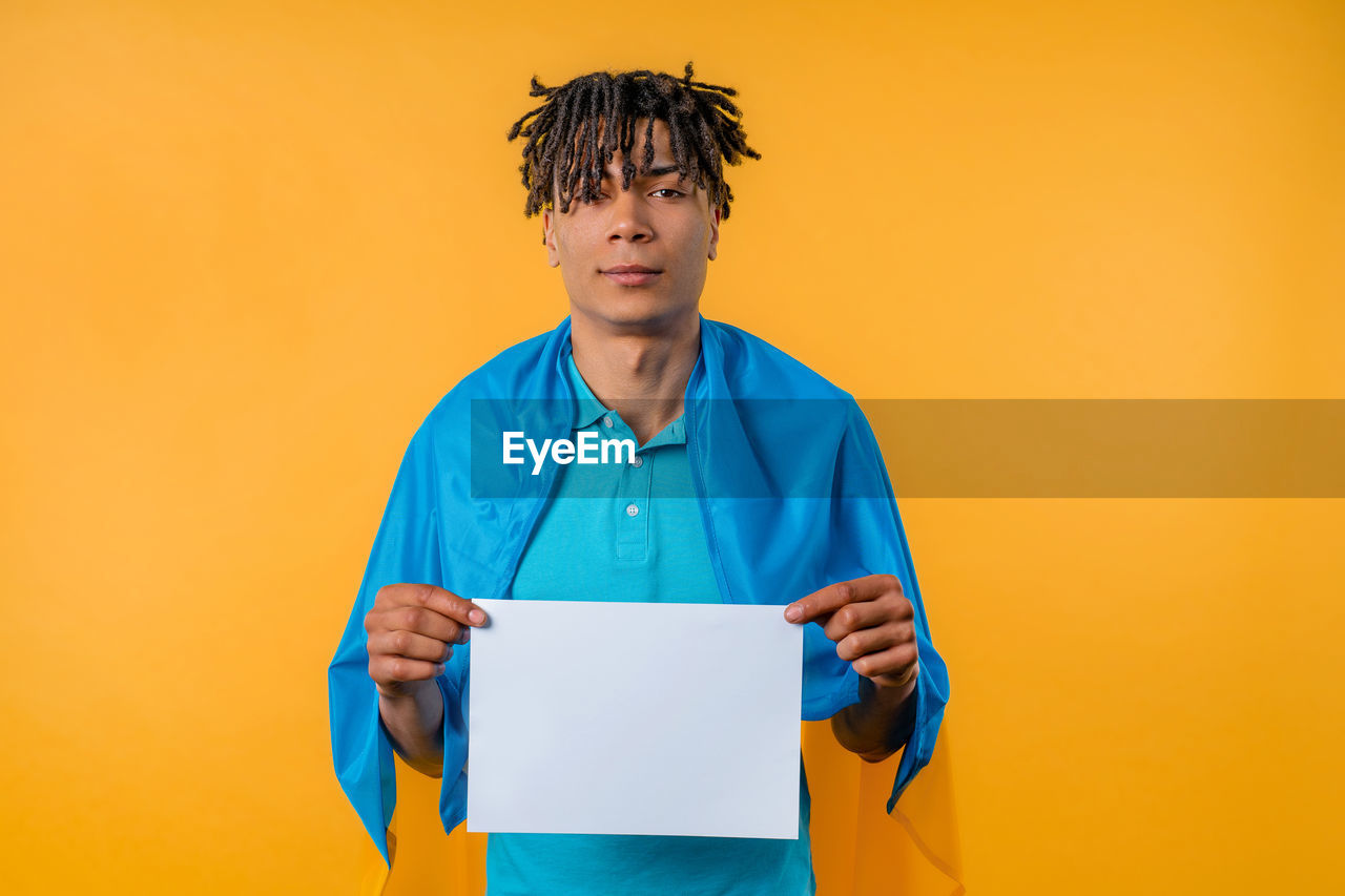 one person, colored background, adult, copy space, studio shot, men, portrait, yellow, indoors, clothing, person, business, occupation, front view, holding, standing, waist up, yellow background, looking at camera, blue, technology, communication, working, business finance and industry, paper, emotion