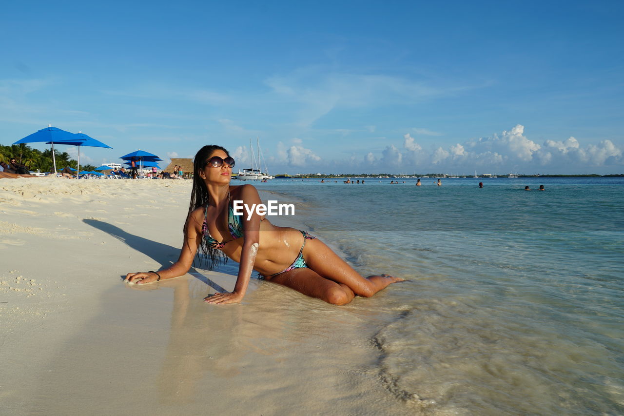 Woman in bikini lying at beach against sky