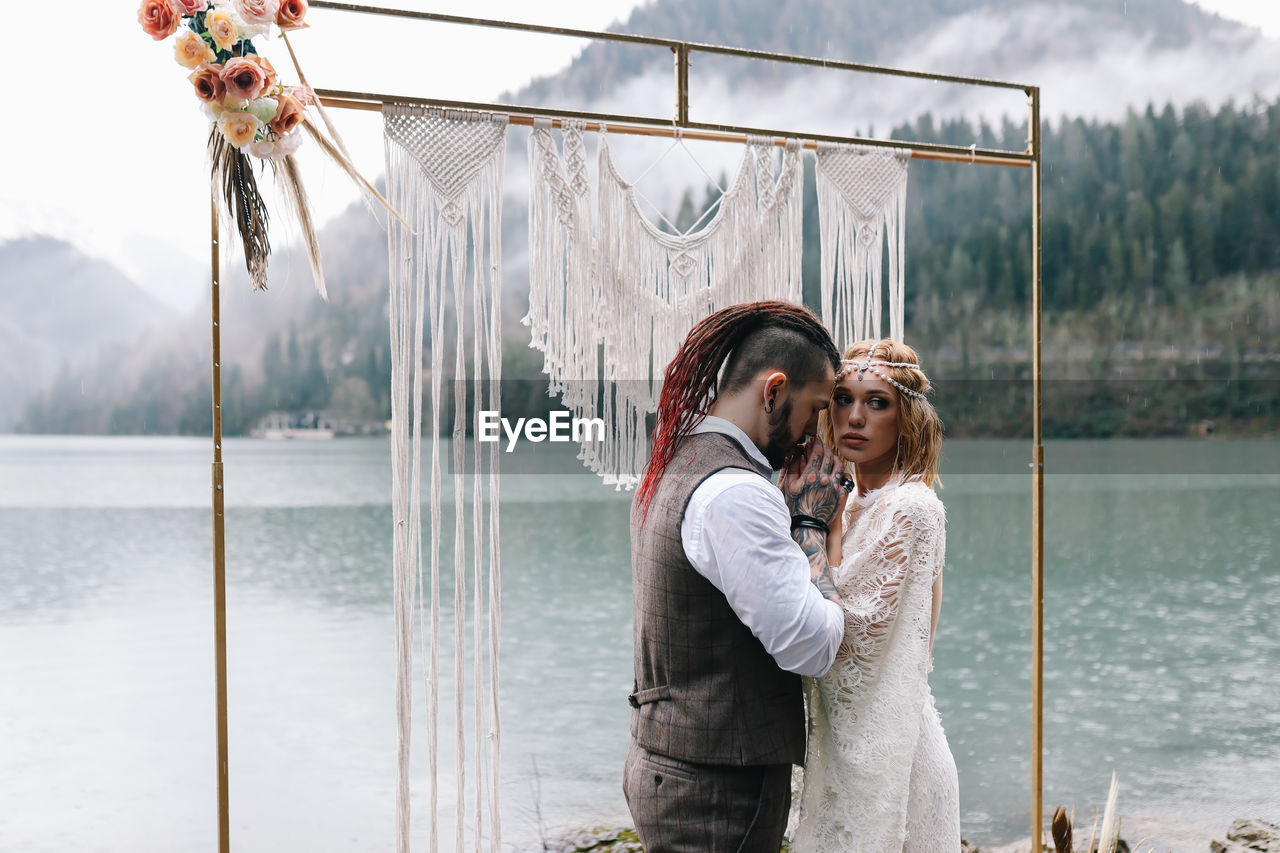 A loving married couple the bride and groom in suits celebrate wedding near the mountains and water