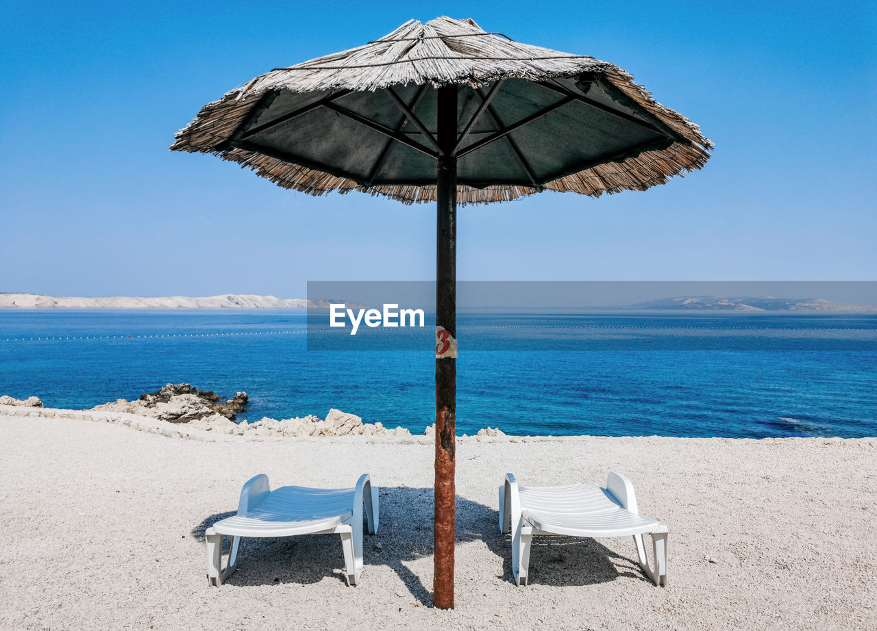 Empty deck chairs under straw parasol on beach on sunny day in summer.