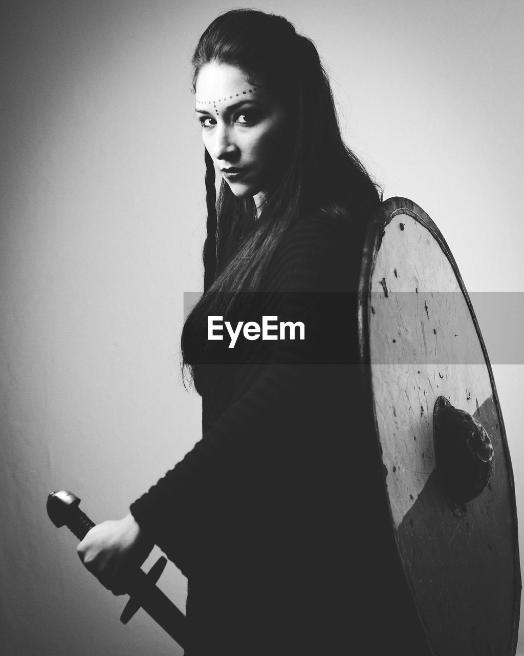 Portrait of confident young woman holding shield and sword