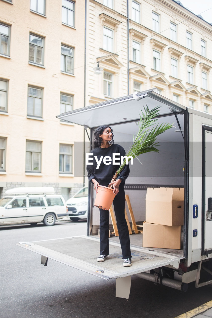 Female mover unloading potted plant from truck on street in city