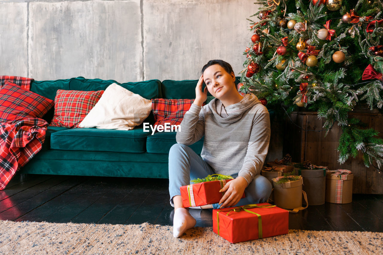 A young woman with a gift for christmas or new year, sits at home on the floor