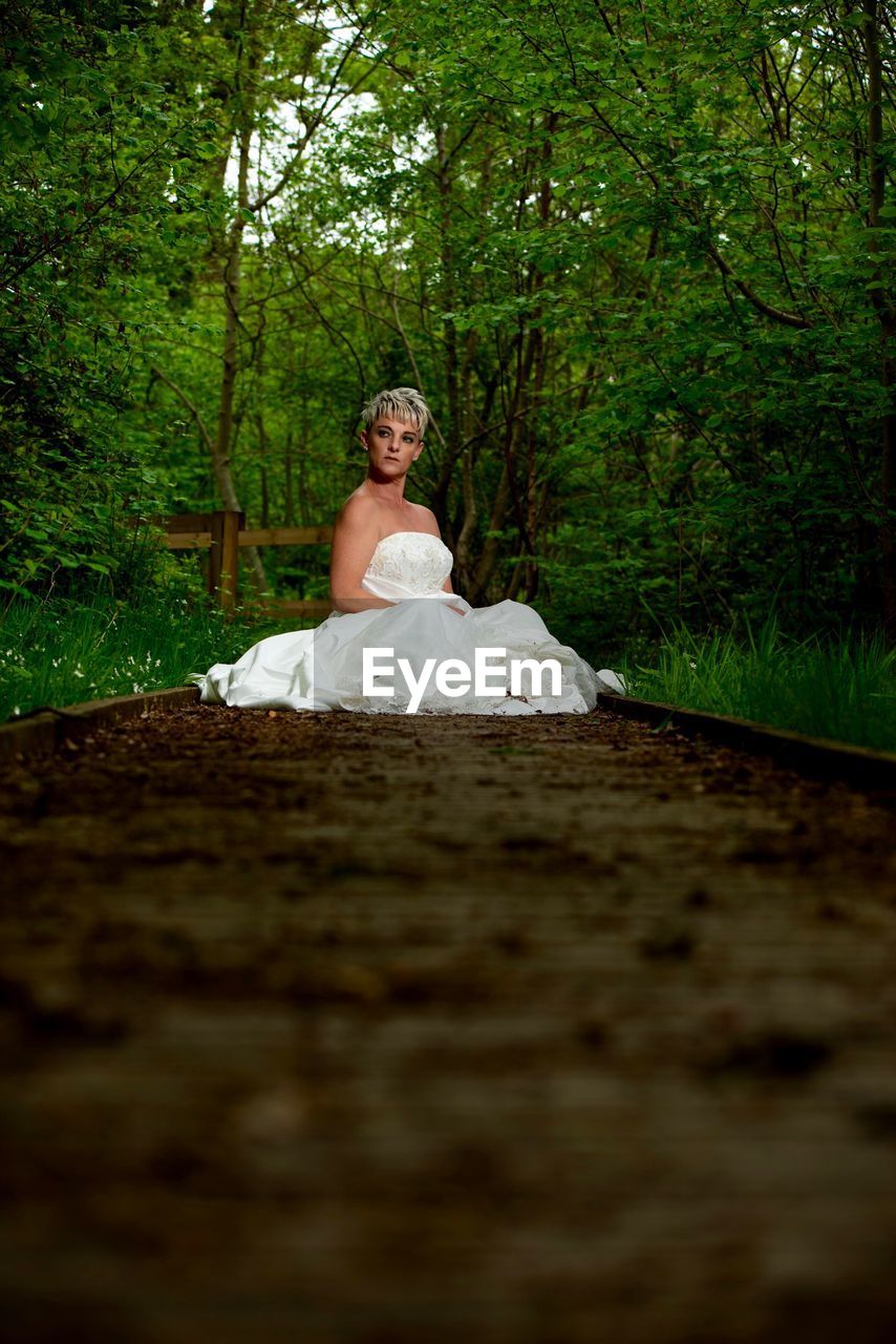 Portrait of bride sitting on dirt road in forest