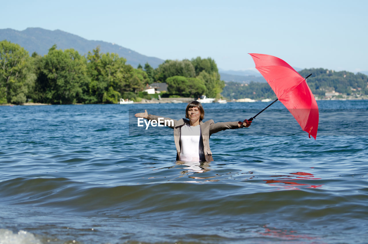 Woman holding umbrella while standing in sea against sky