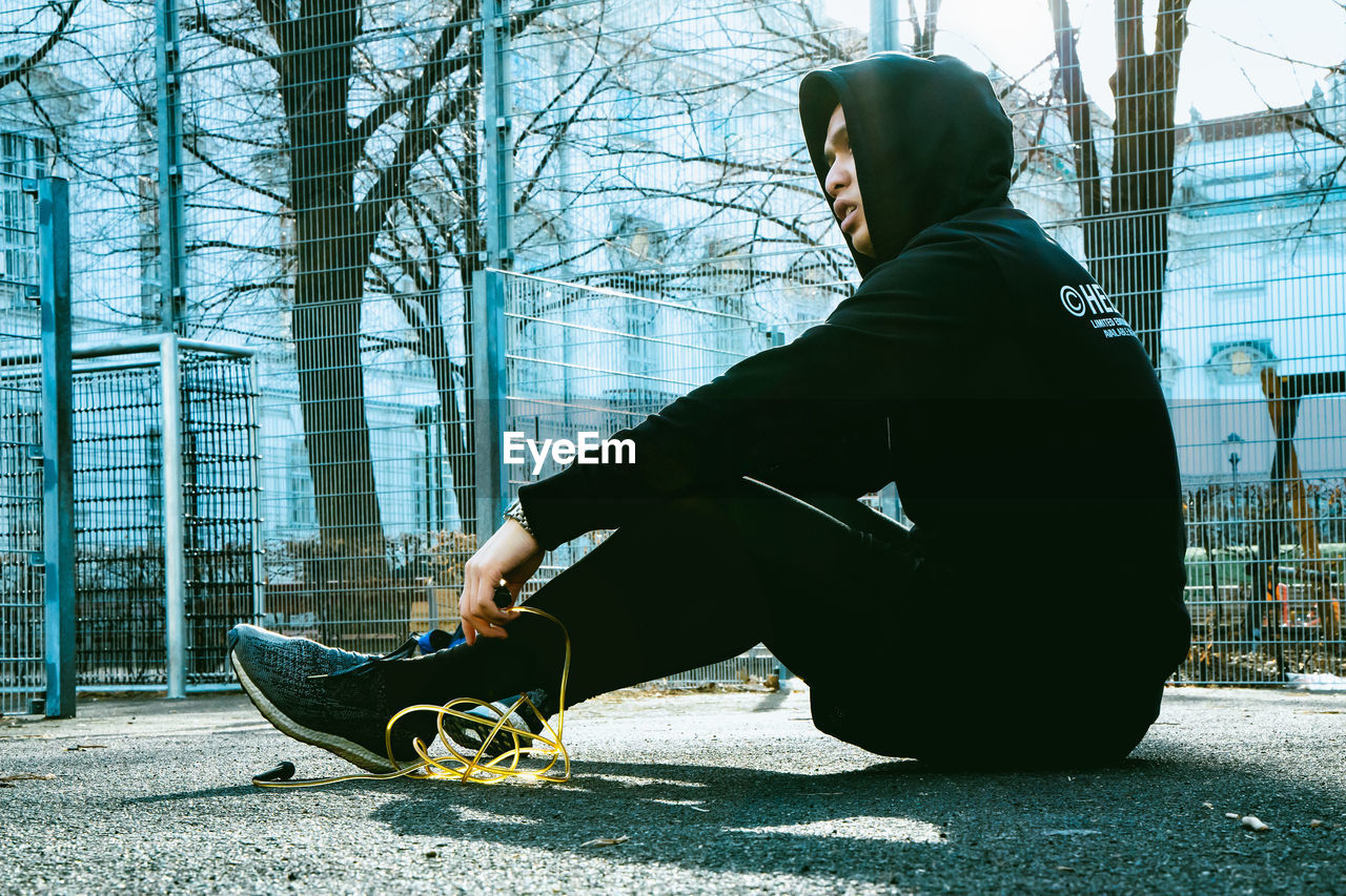 SIDE VIEW OF MAN SITTING ON SIDEWALK