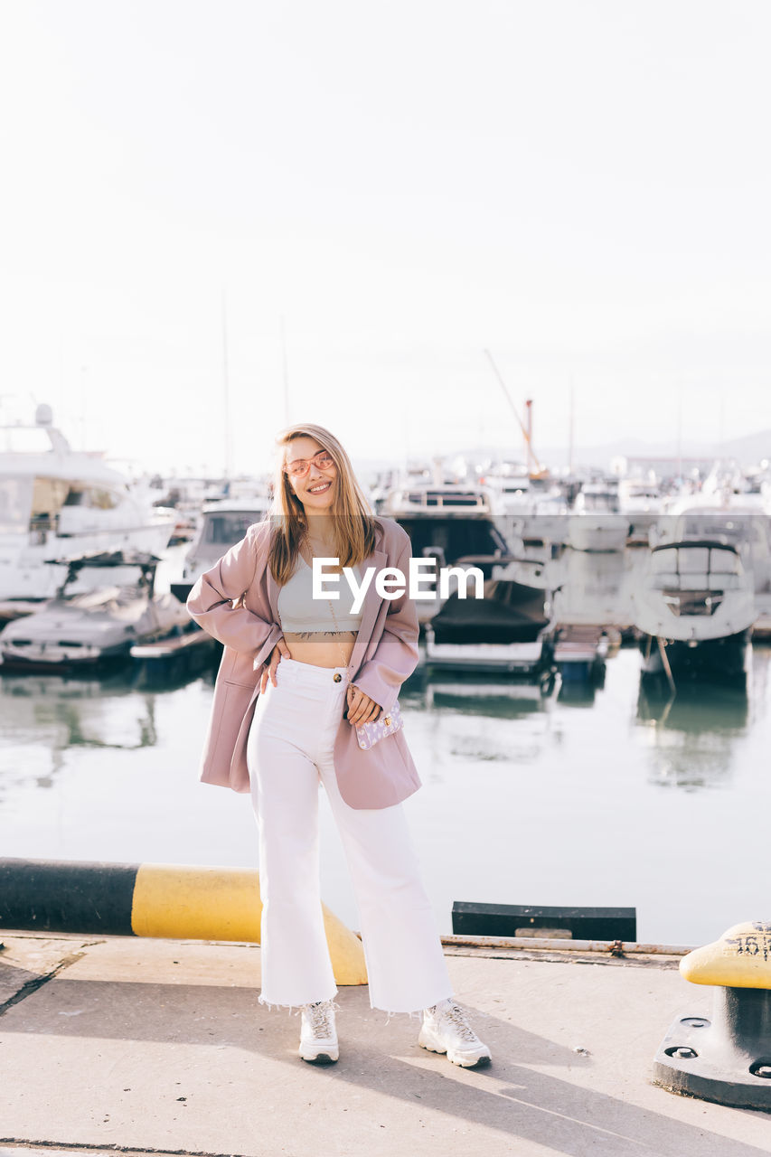 Portrait of a happy cheerful emotional traveling girl in fashionable clothes near yachts and water