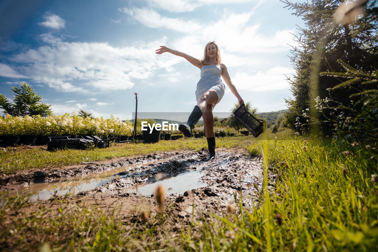 WOMAN JUMPING ON FIELD AGAINST SKY