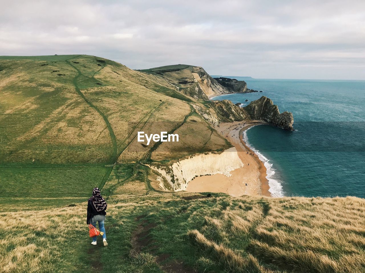 Rear view of woman standing on hill by sea against cloudy sky
