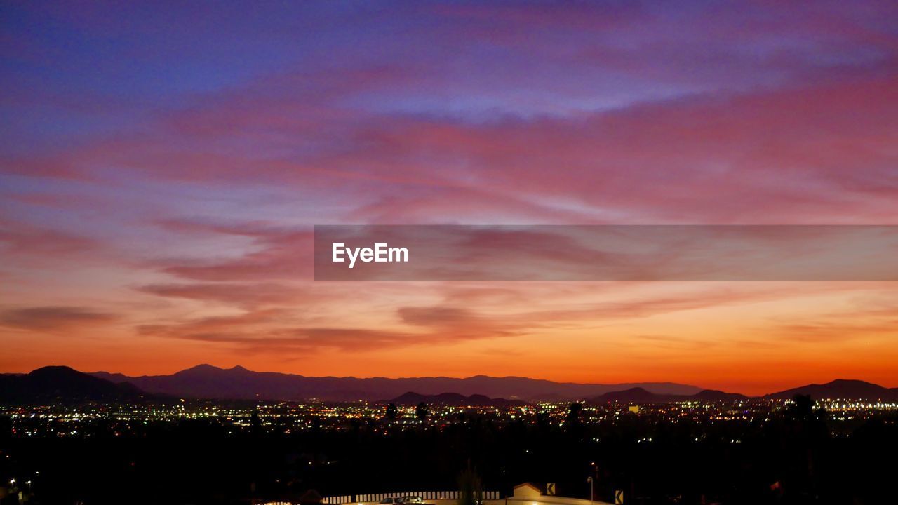 Illuminated cityscape against sky during sunset