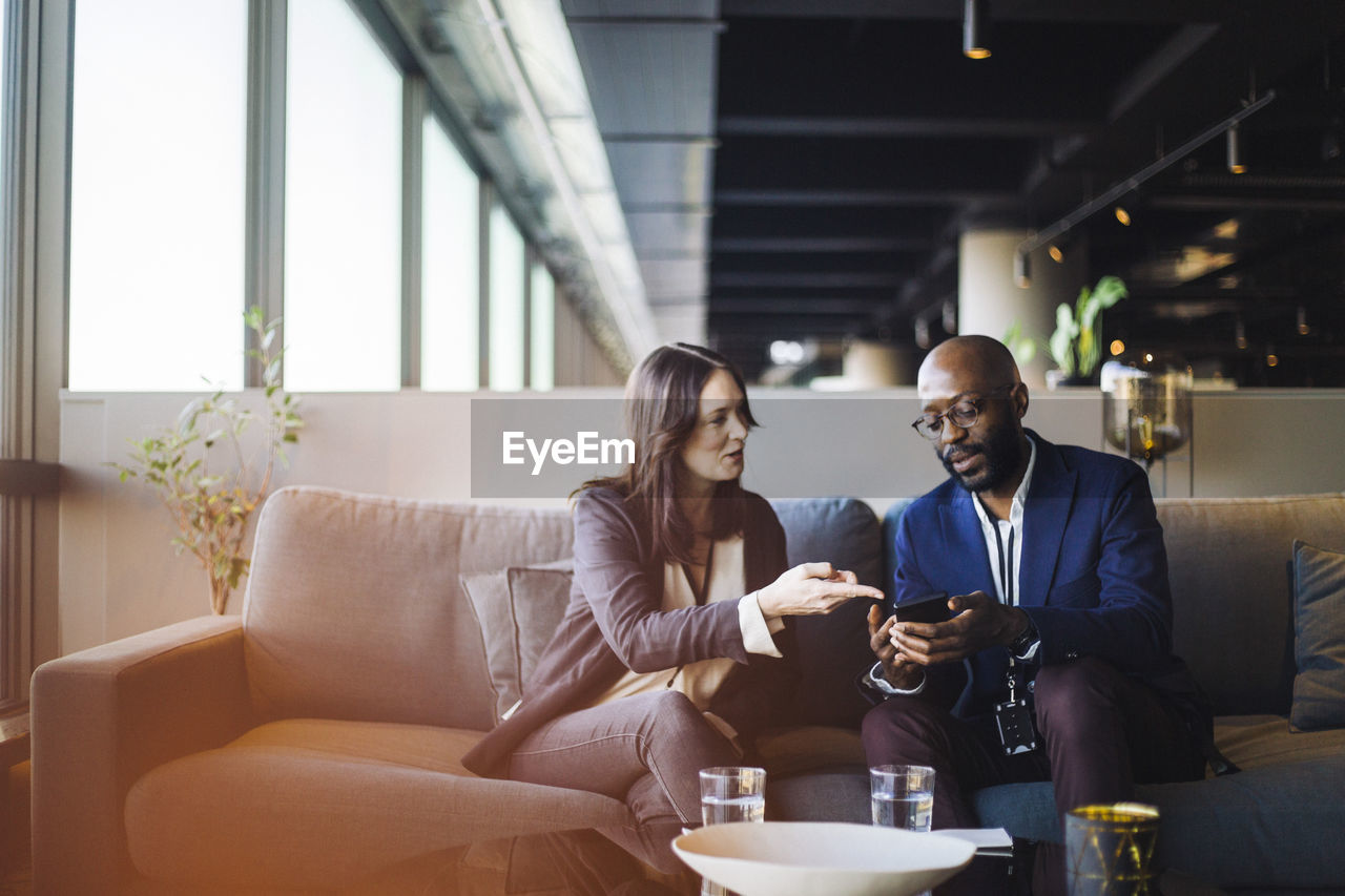 Businessman showing smart phone to businesswoman while sitting in office