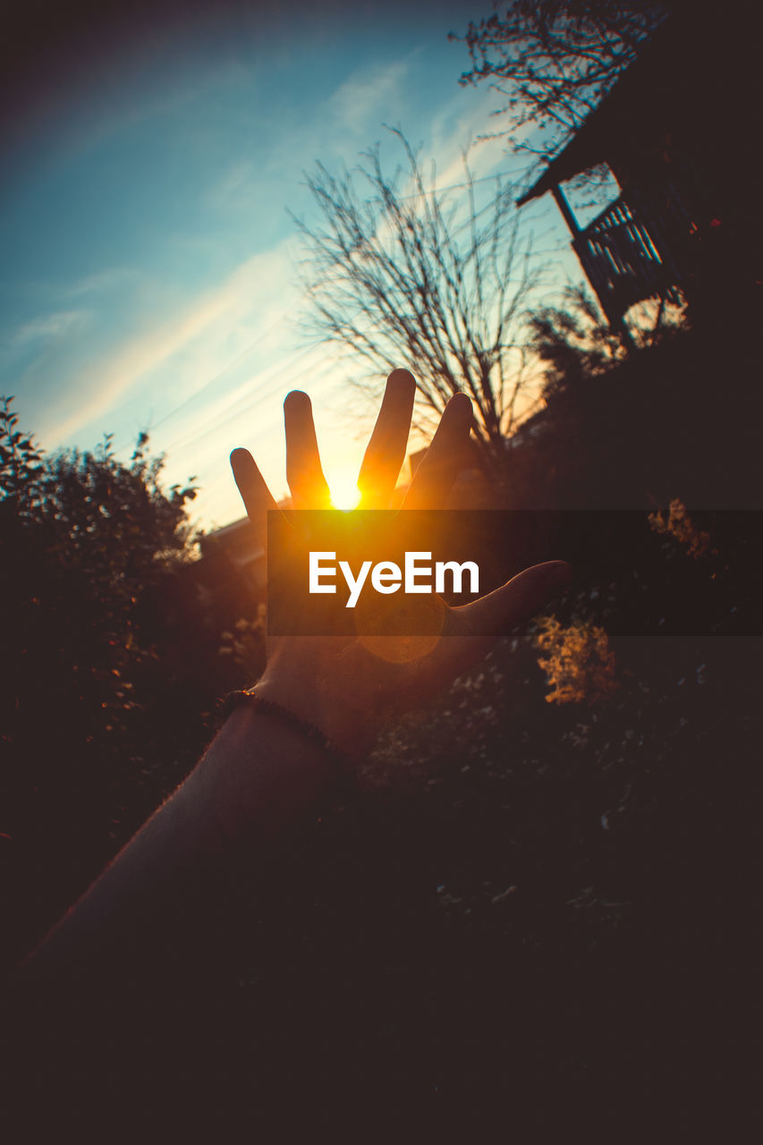 Cropped hand of person against sky during sunset