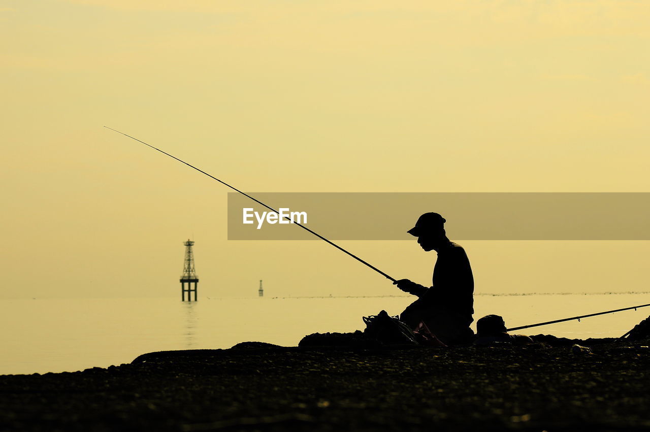 Silhouette man fishing at sunset