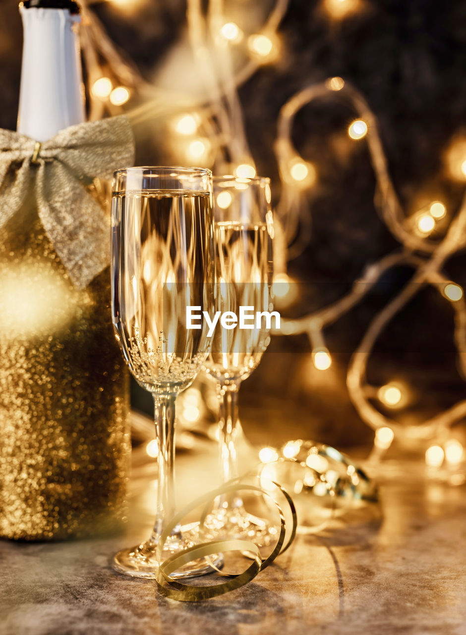 New years eve dark party table with two champagne flute, shiny bottle and christmas lights