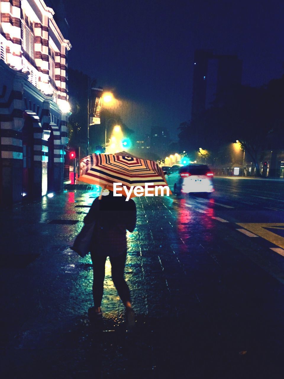 Rear view of woman holding umbrella and standing on wet street