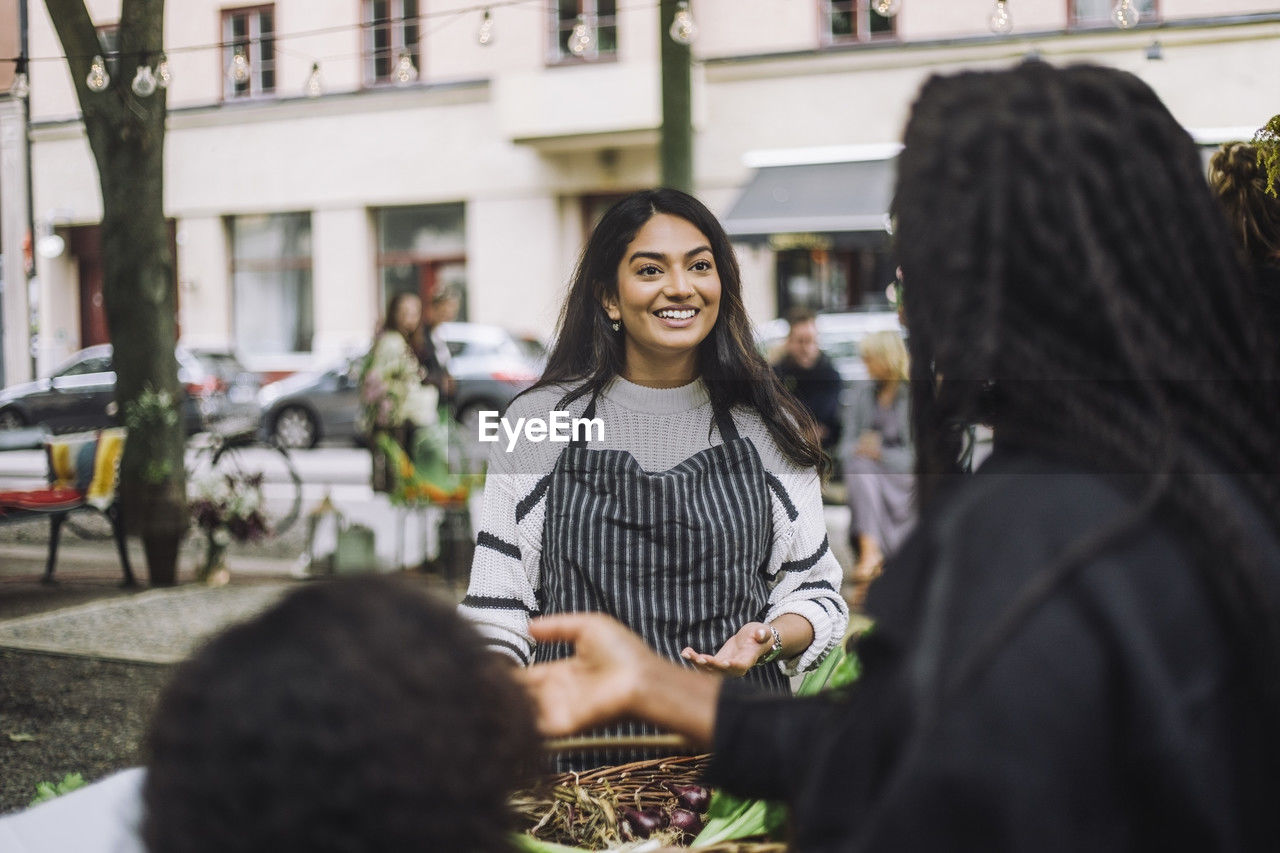 Smiling female vendor talking with customer doing shopping at farmer's market