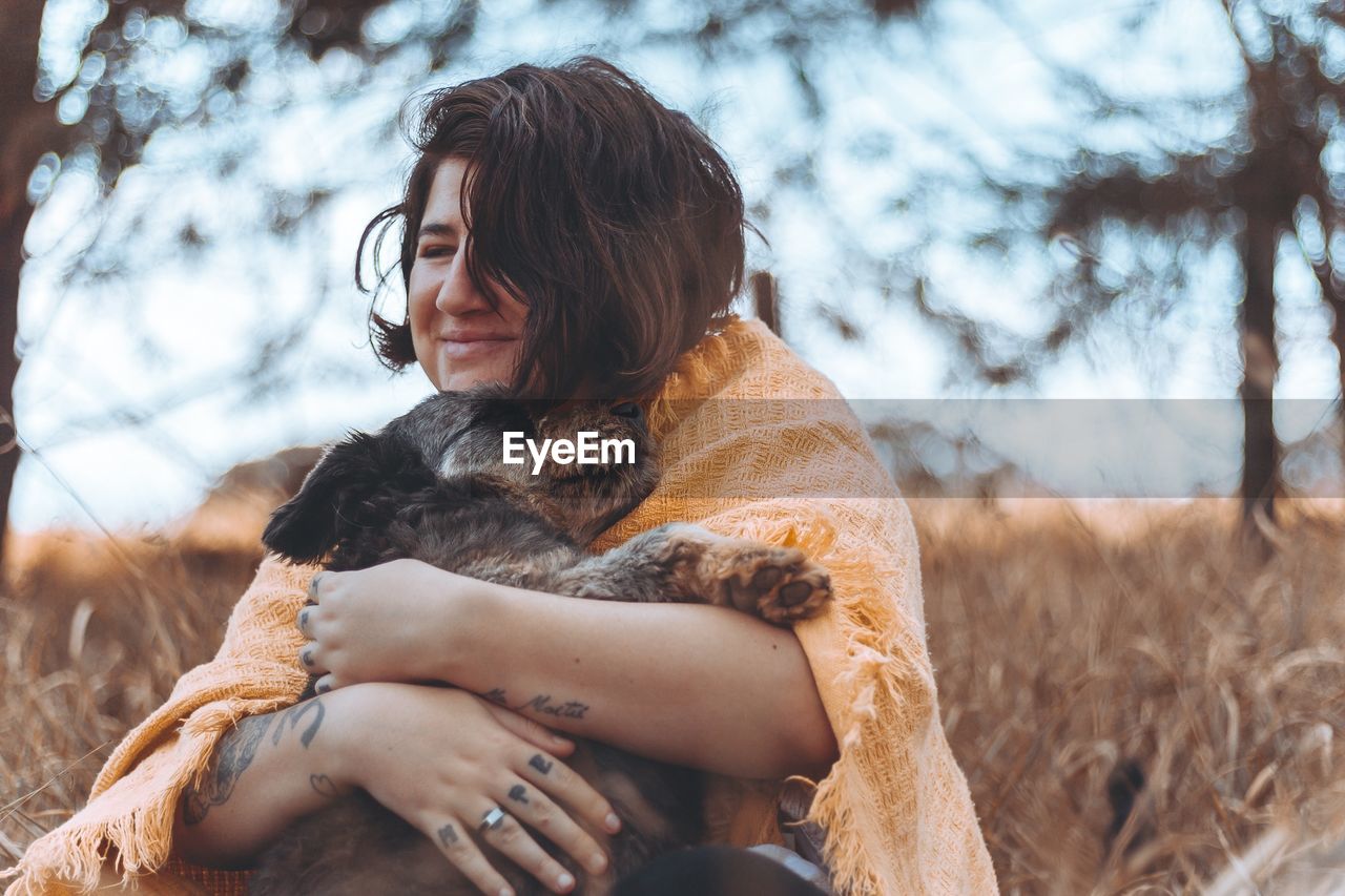 Smiling young woman embracing dog on field