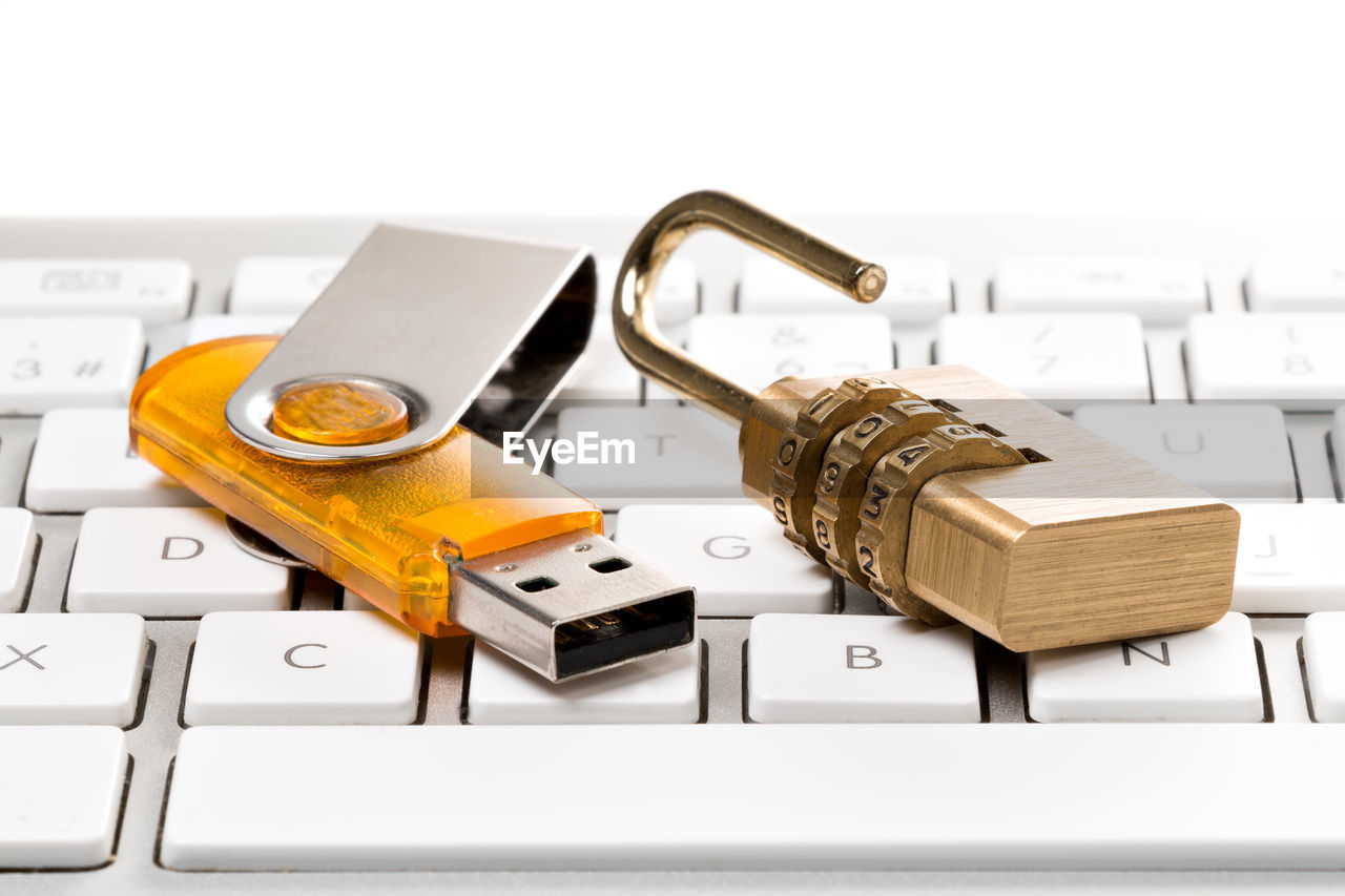 Close-up of padlock and usb stick on computer keyboard against white background