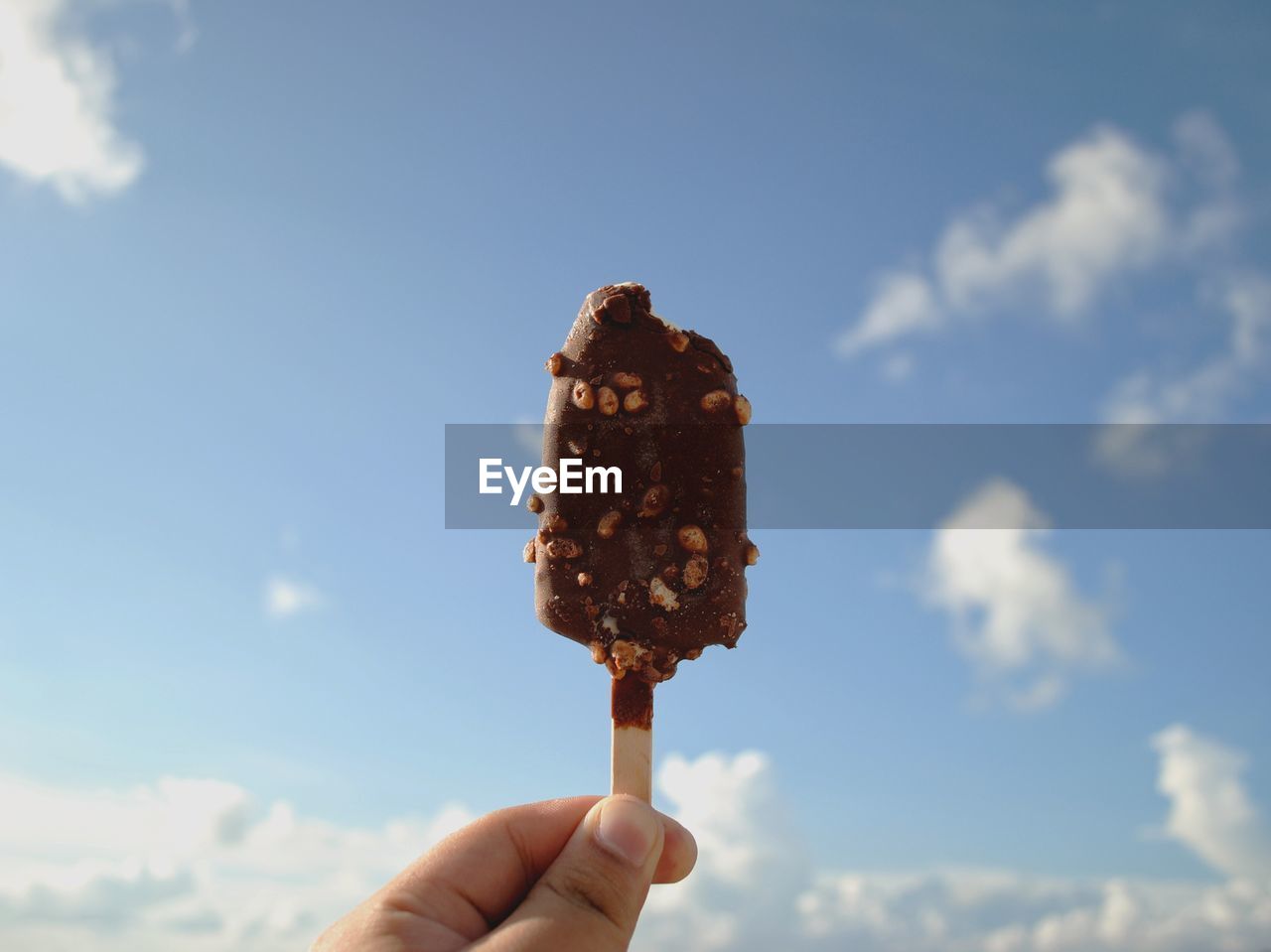 Midsection of person holding ice cream against sky