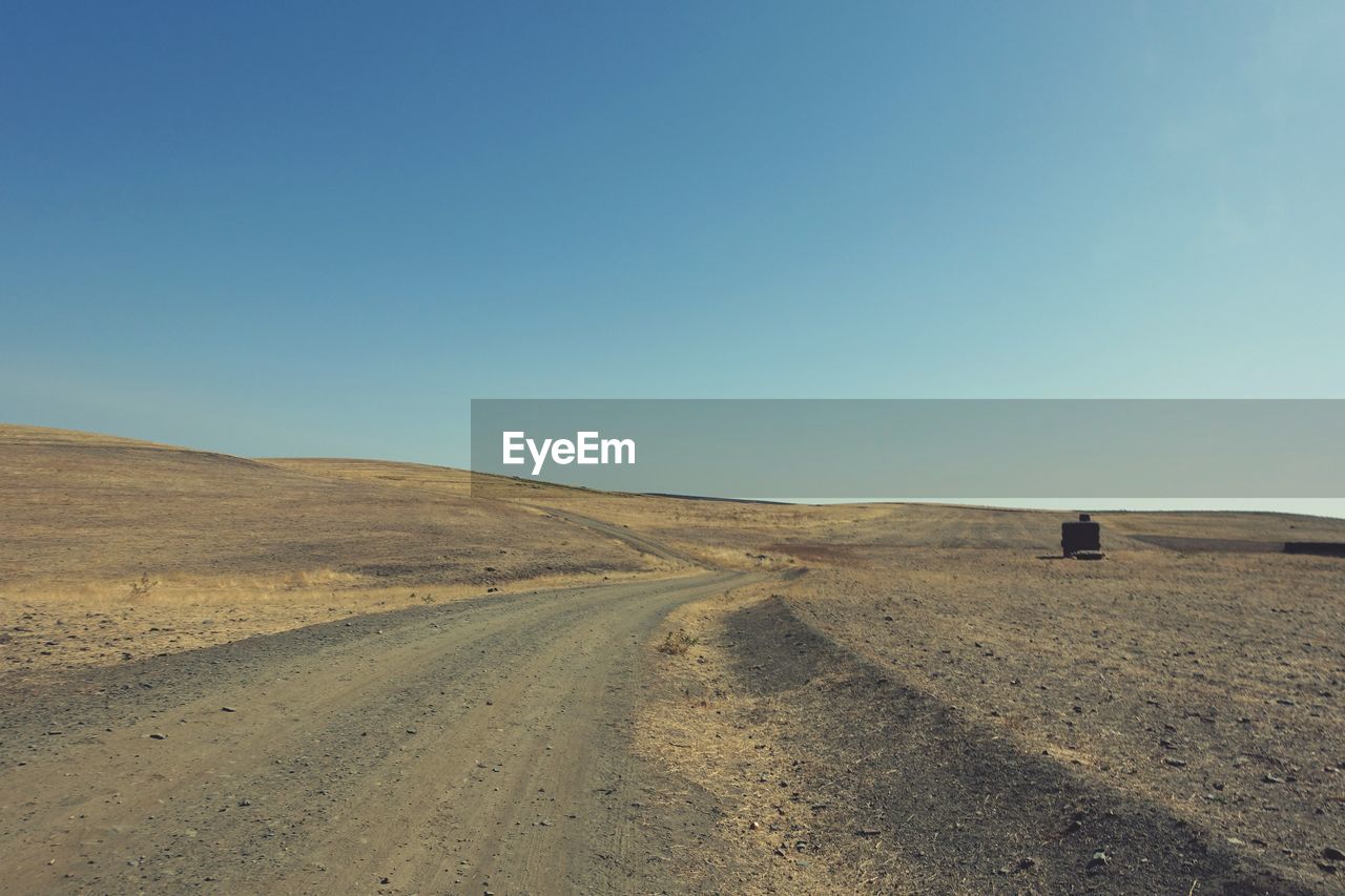 Road amidst desert against clear blue sky