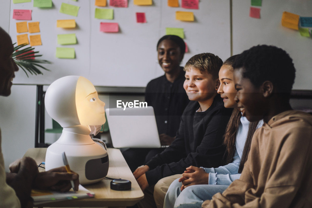 Smiling multiracial students looking at illuminated modern robot in innovation lab