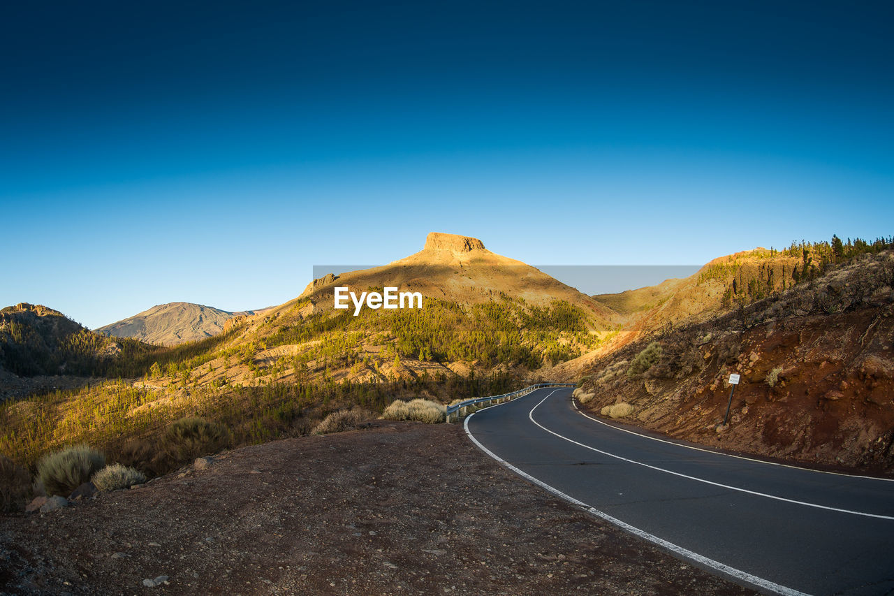 ROAD PASSING THROUGH MOUNTAIN AGAINST BLUE SKY