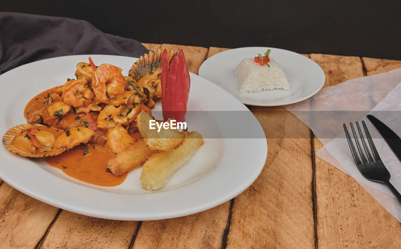 Peruvian food, called pescado a lo macho, wooden table, fish fried in seafood sauce, and rice