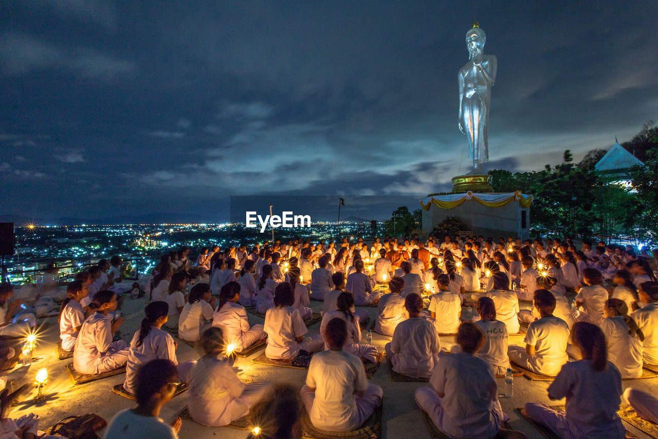 People praying against buddha statue at night