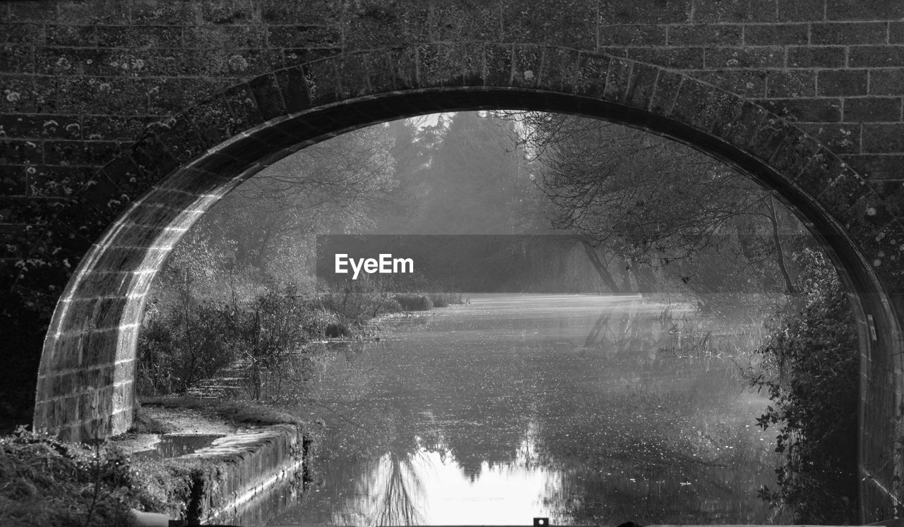 Calm lake along plants seen through arched wall