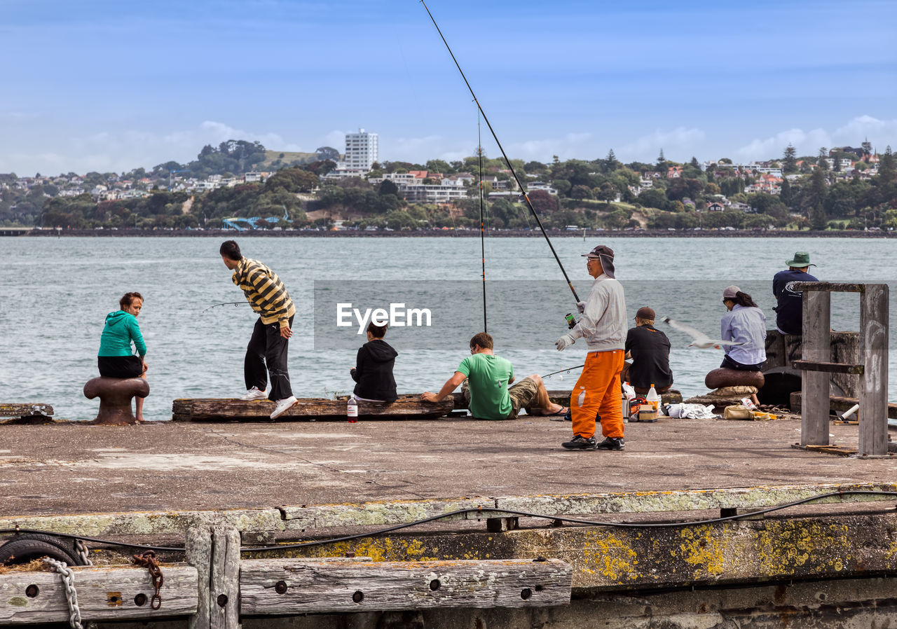 GROUP OF PEOPLE FISHING IN SEA AGAINST CITYSCAPE