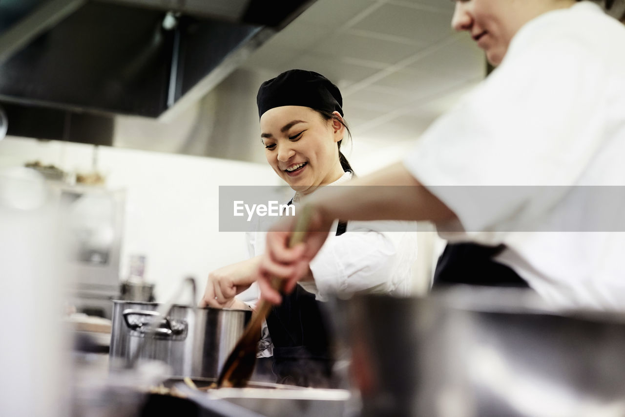 Smiling female chef student with colleague cooking food in commercial kitchen