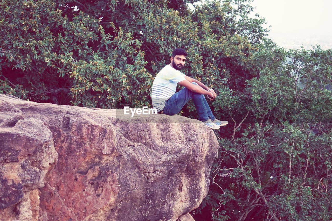 YOUNG MAN SITTING ON ROCK BY TREE