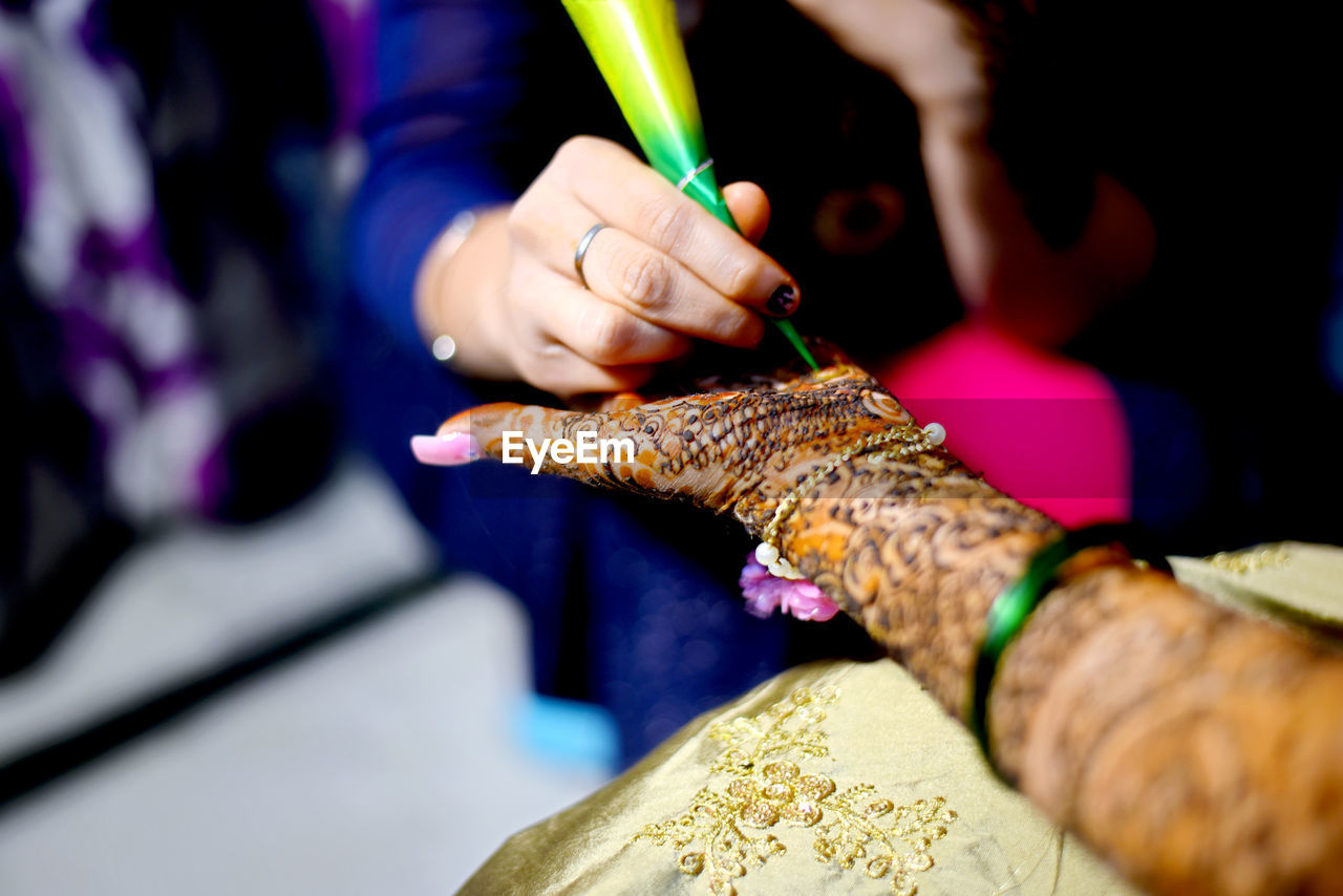 Midsection of woman making henna tattoo on friend palm