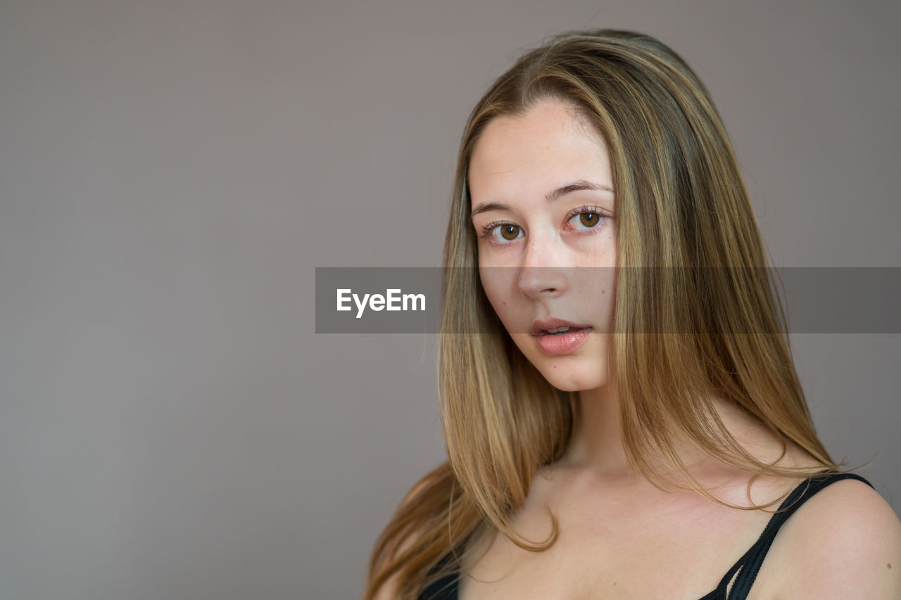 Portrait of an attractive teenage girl wearing camisole posing looking at camera on grey background