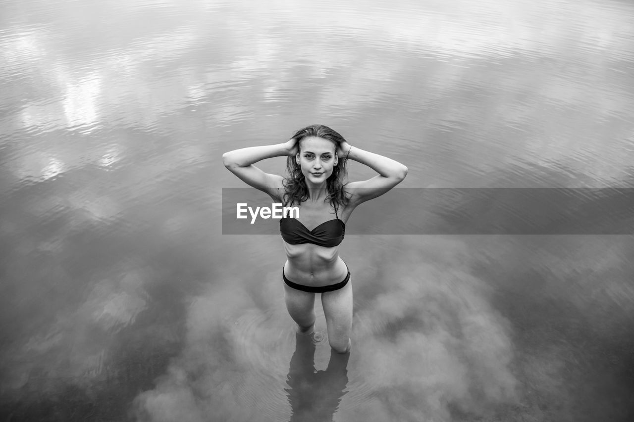 High angle portrait of young woman wearing bikini standing in lake