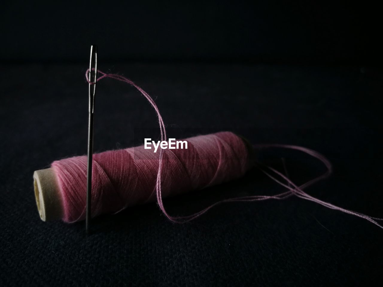 Close-up of thread spool with needle against black background