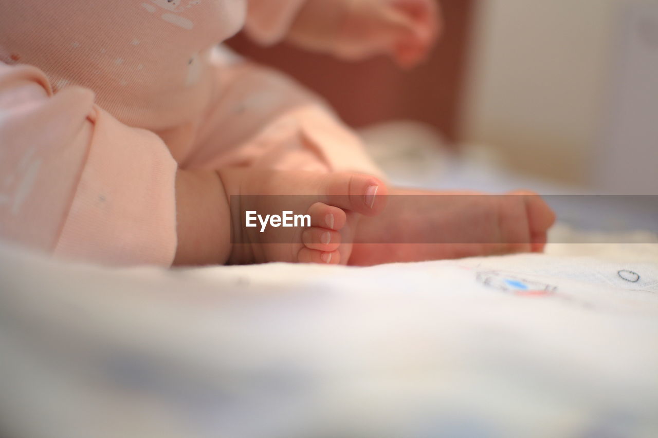 Low section of baby girl sitting on bed at home