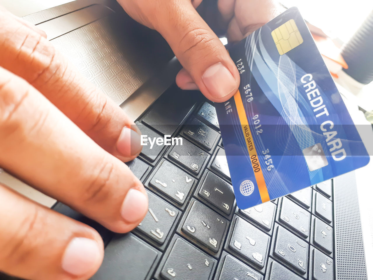 Close-up of hand holding credit card on laptop