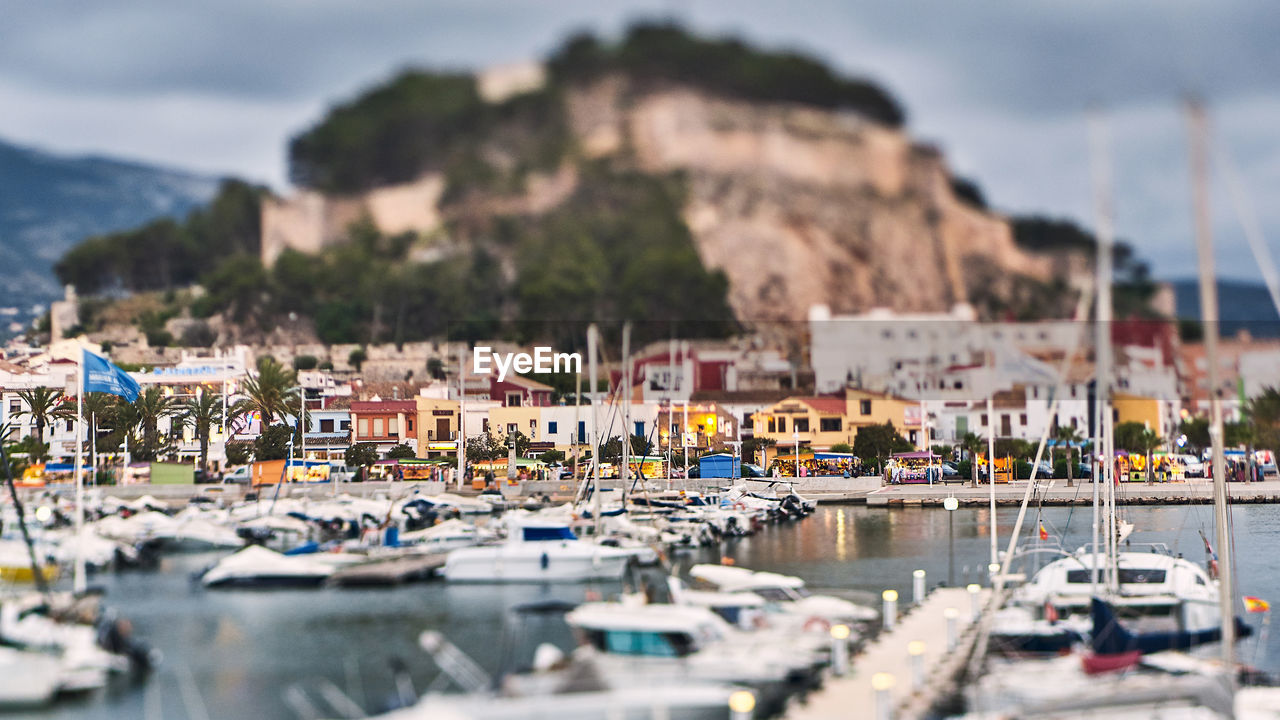 SAILBOATS MOORED AT HARBOR AGAINST BUILDINGS IN CITY