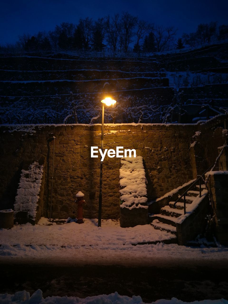 Illuminated street light by frozen lake against sky at night