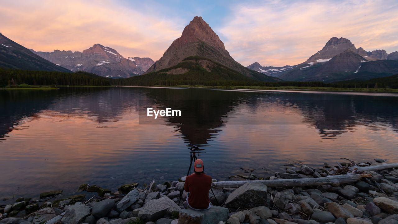 Rear view of man photographing mountain by lake at dawn