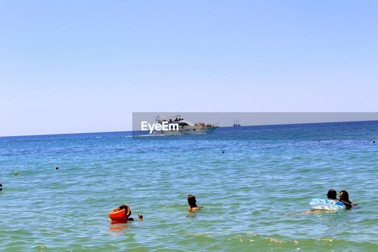 VIEW OF PEOPLE SWIMMING IN SEA AGAINST CLEAR SKY