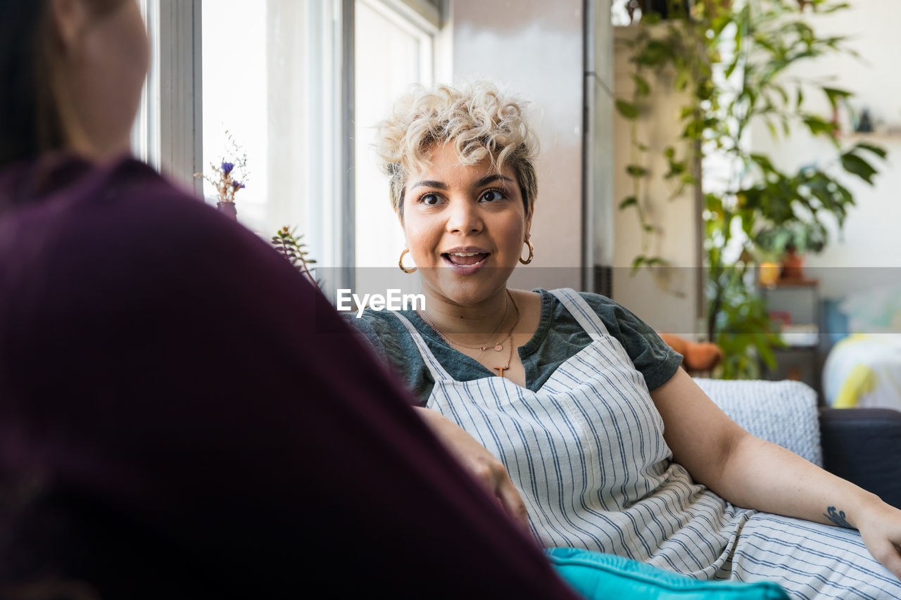 Mid adult woman talking to friend while sitting on sofa at home