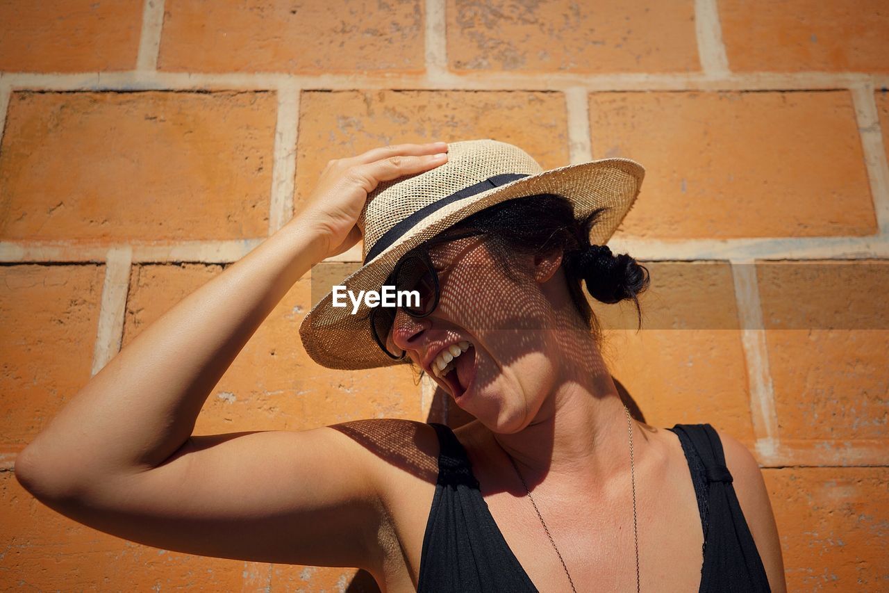 Cheerful woman wearing hat against brick wall