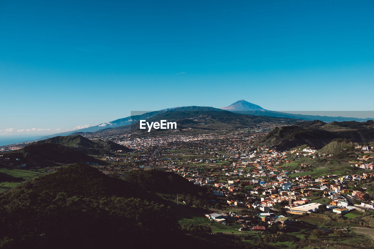 Aerial view of townscape by mountain against blue sky