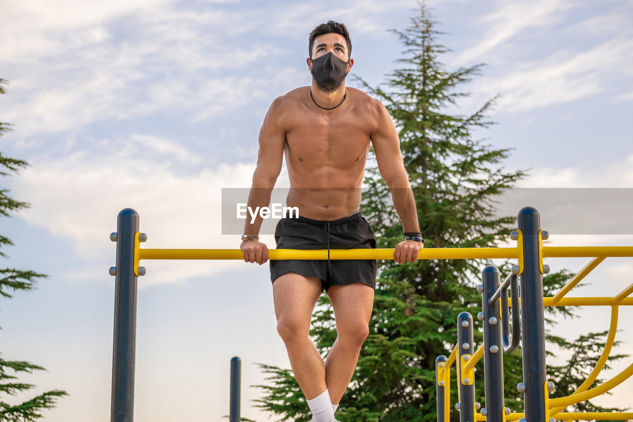 Full length of shirtless man sitting on railing