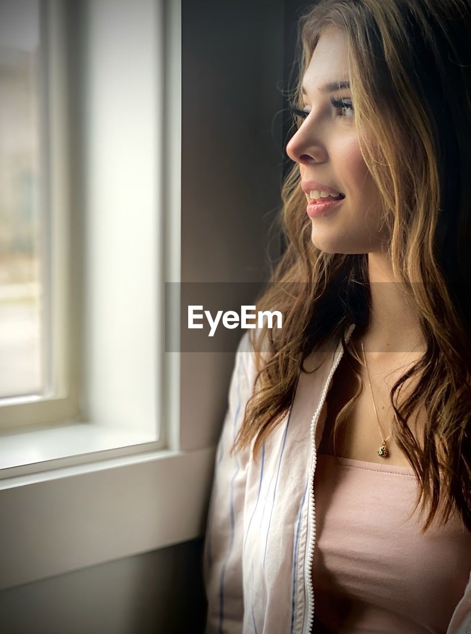 Three-quarter profile view of a beautiful young woman looking through a window.
